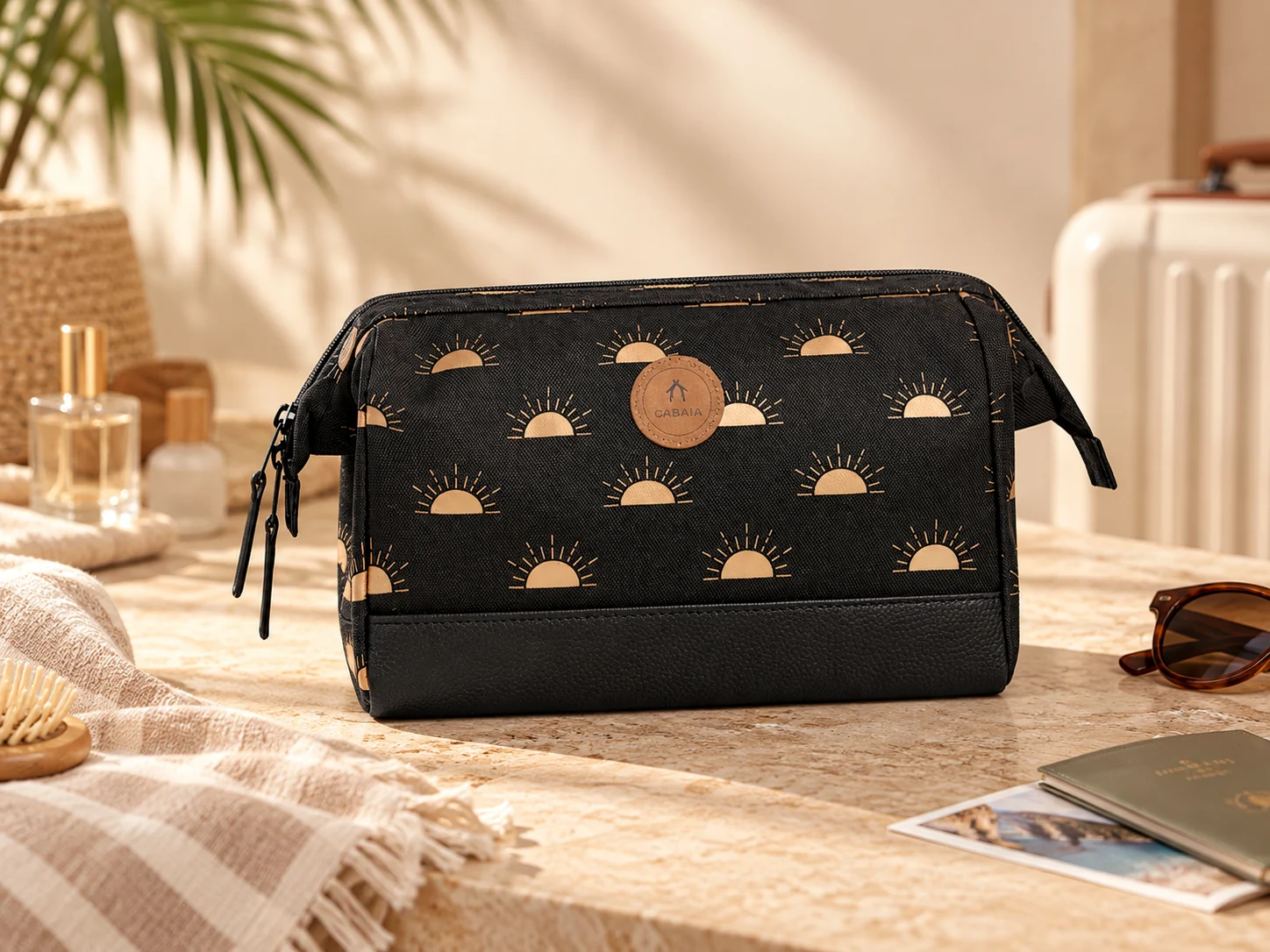 Mise en scène de la trousse de voyage CABAIA près d'une valise, de lunettes et de produits de toilette